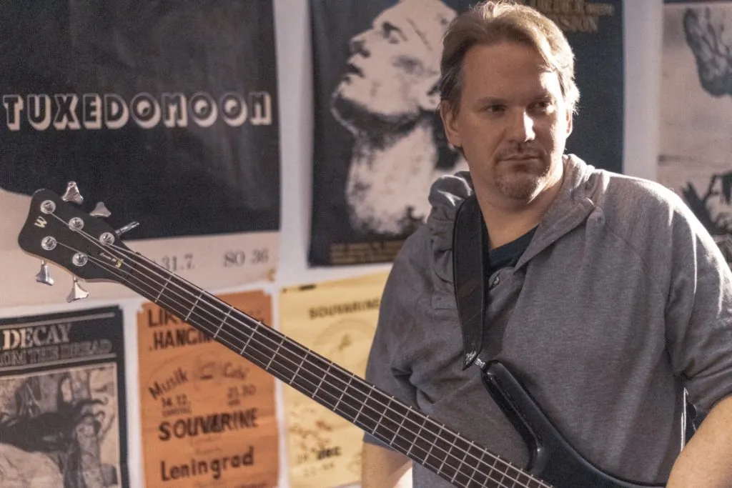 Michael mit Bass vor alten Konzertplakaten im Proberaum